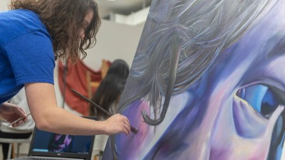 a student paints on a large canvas an up-close portrait.