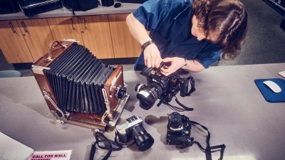 An overhead view of a Cage employee with modern and antique camera equipment spread on a counter.