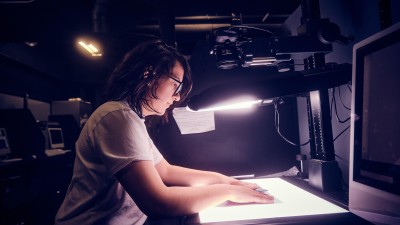 a student adjusts a piece of paper under lights and an overhead camera.