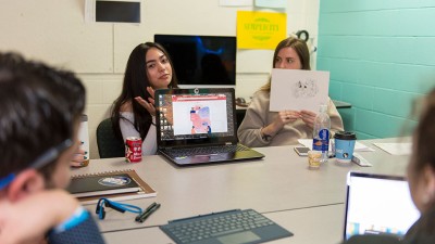 two students display artwork to the rest of the class.