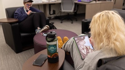 two students drawing on tablets in a lounge area.
