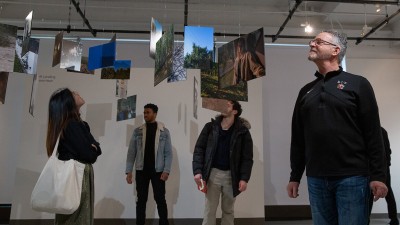 Exhibition attendees take in photos that are suspended from the ceiling. 
