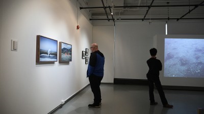 Exhibition attendees look at still photos and a video installation. 