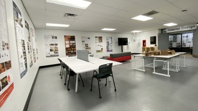 Tables, chairs, models and printed posters displayed in a hallway space.