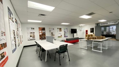 Tables, chairs, models and printed posters displayed in a hallway space.