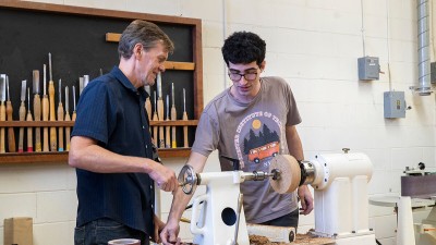 faculty member helps a student with a lathe project.