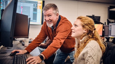 Faculty Craig Foster works at a computer with a student.