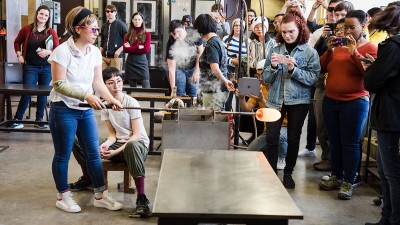 a visiting artist leads a demo in the hot shop for a group of people.