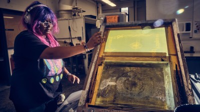 A student holds up a large print plate in the studio.