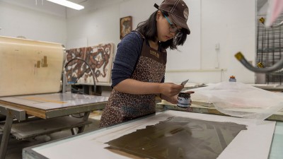 a student wearing an apron spreads a black paste over a print.