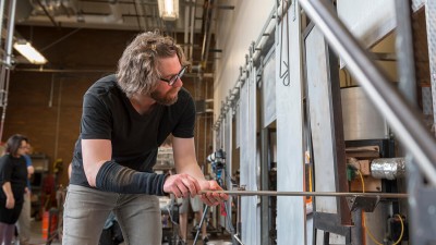 a faculty member sticks a glass object into one of the hot shop's ovens.