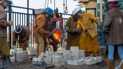 Faculty and students wearing protective gear while pouring molten iron into brick molds.