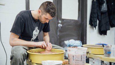 a student spins a flat piece of clay on a wheel.
