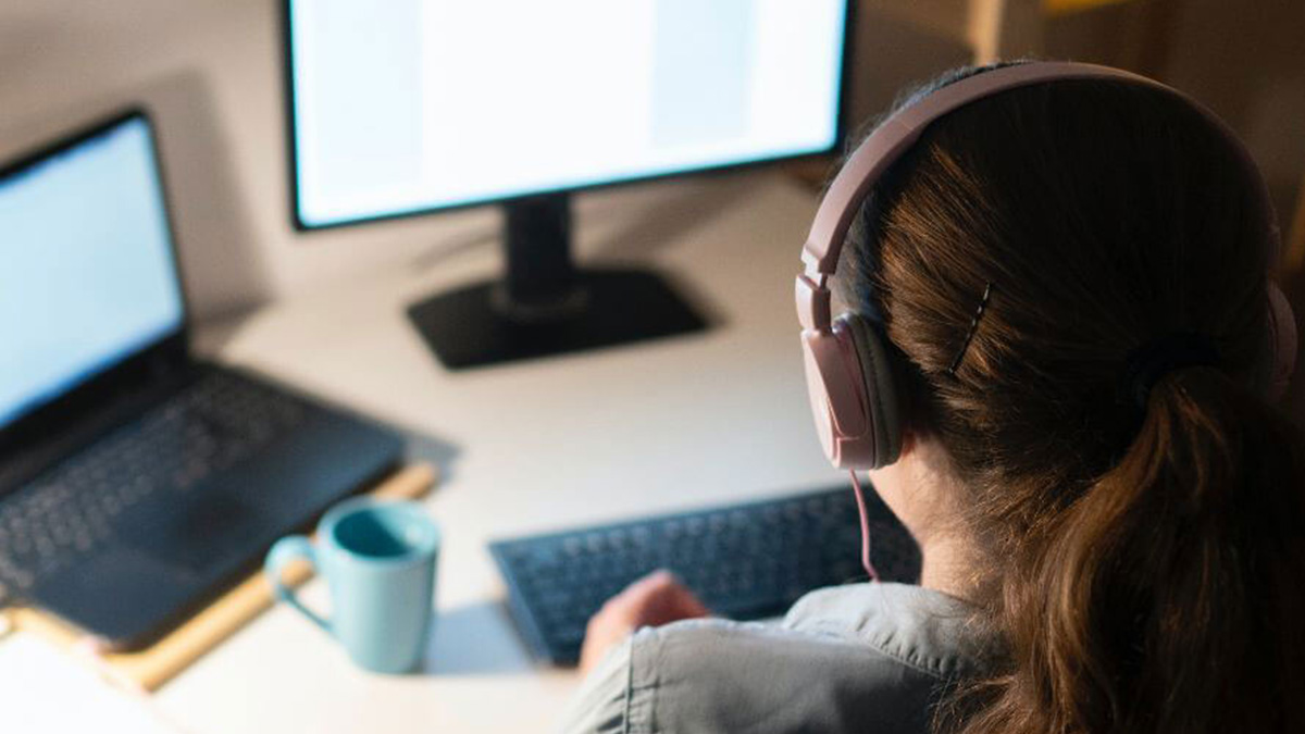 A person wearing headphones sitting at a desk working on a computer.