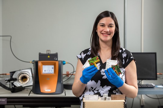 Meredith Noyes stands at a work bench showing some of the 3D printed samples