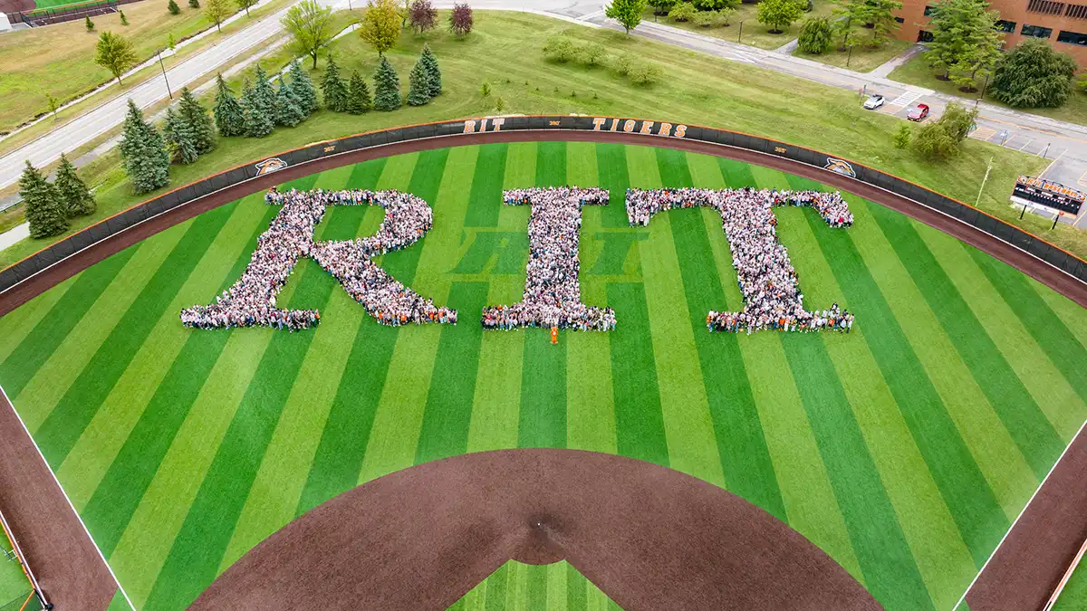 The incoming freshmen class forms the letters 'R I T' on a striped baseball field.