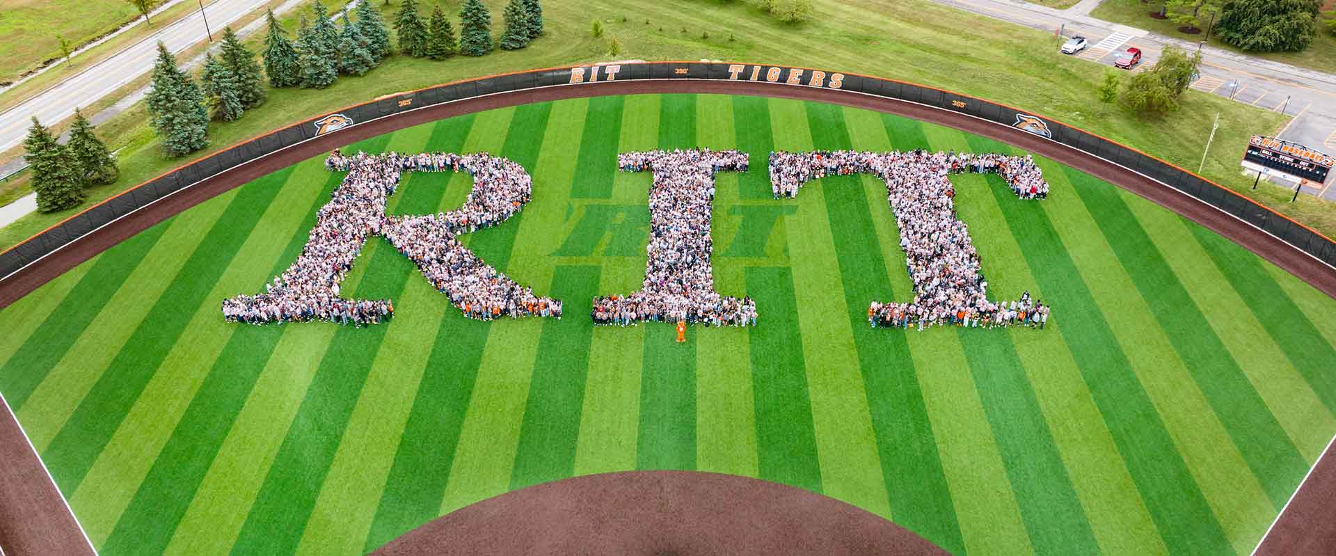 The incoming freshmen class forms the letters 'R I T' on a striped baseball field.