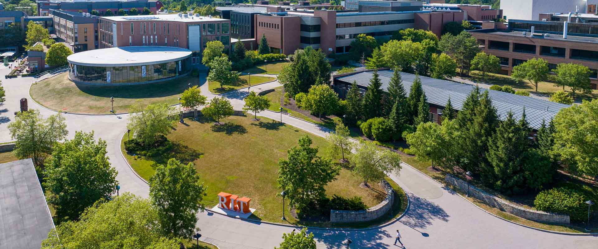 An aerial view of R I T’s campus shows modern brick buildings, green spaces, and large orange 'R I T' letters.
