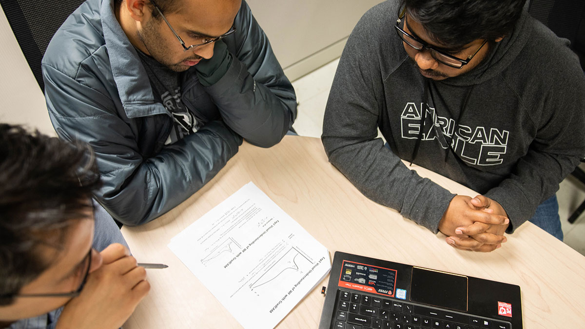 professor and two students examining a problem on a worksheet.