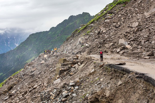 a rock landslide is shown with a man taking a photo in the foreground and mountains in the background.