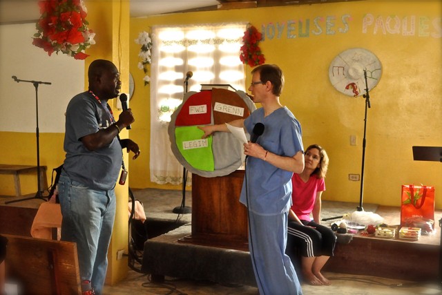 two men stand in front of a spinning wheel with options on it.