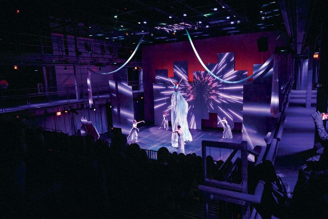 Performers bathed in white and purple lights dance around a stage.