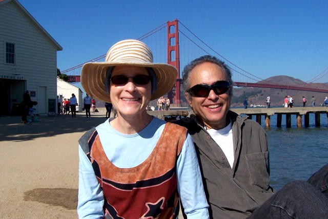 Smiling couple poses by the water with the Golden Gate Bridge in the background.