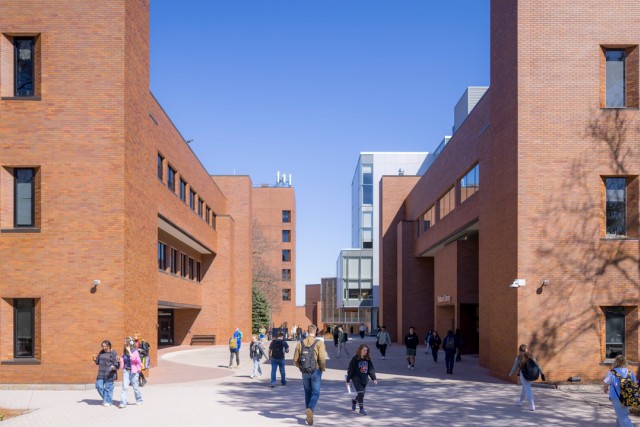 Students walk between brick buildings.