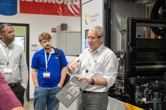  Man presenting a manufactured part to a group during a factory tour or workshop.