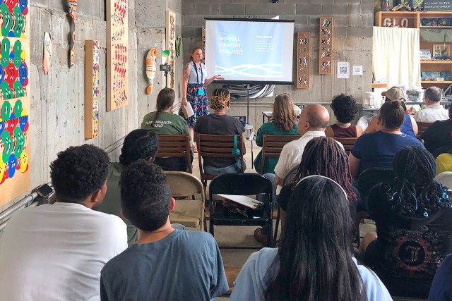 a woman stands in front of a room of people giving a presentation.