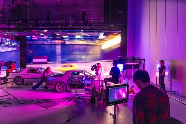 a film crew stages two cars on a purple-lit virtual production set with a moving LED backdrop