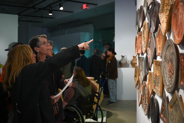 Gallery visitors point at ceramic plates in City Art Space.