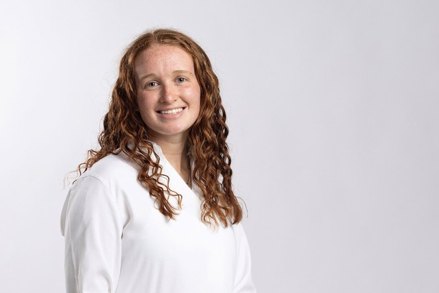 a headshot of a college age female with curle red hair and a white shirt on a white background.