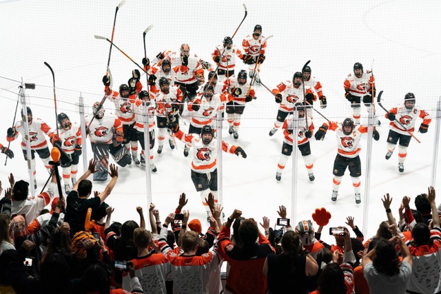 the R I T womens hockey team celebrates with sticks up on the ice.