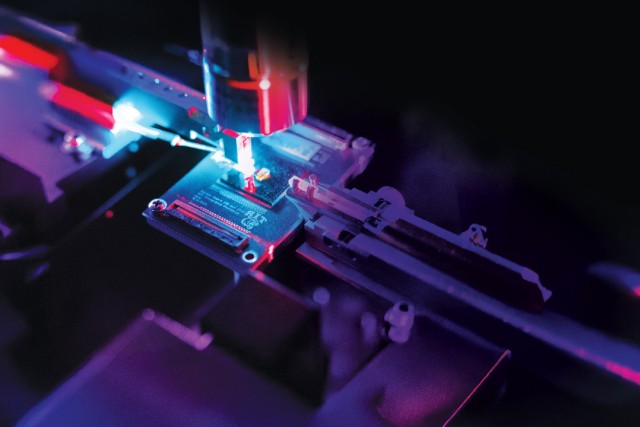 Robotic arm places component on circuit board under neon lighting.