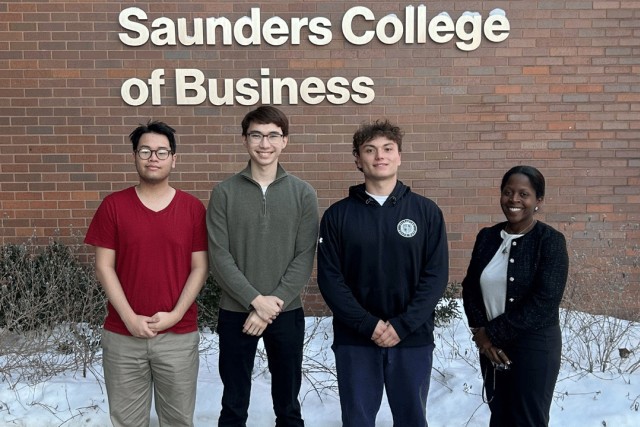 a group of four people stand in front of a brick building labeled Saunders College of Business