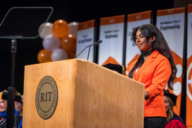 a student orange blazer as she welcomes the audience at the Gordon Field House and Activities Center for New Student Convocation