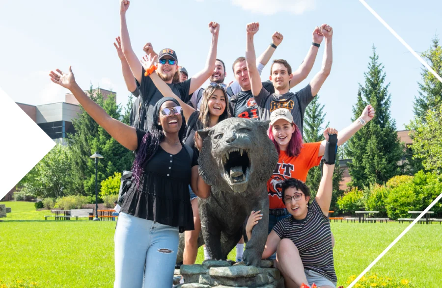 Students with their arms raised in the air posing around the RIT tiger statue