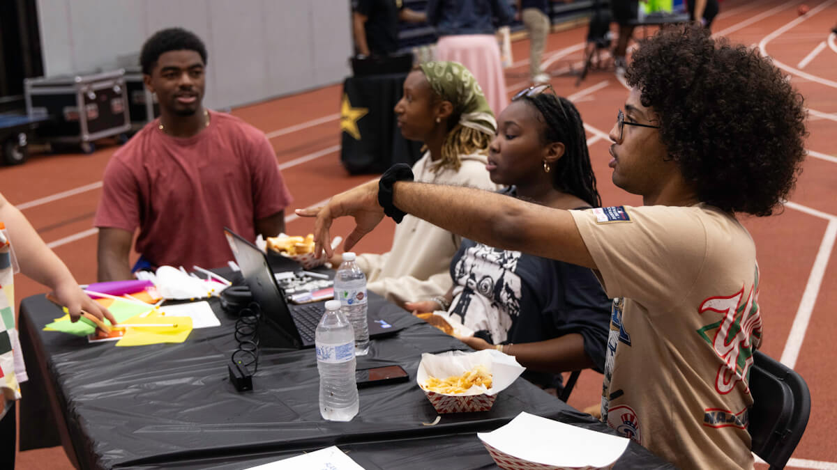 Four students of the ALANA Collegiate Association sit at a table and talk in the Gordon Field House