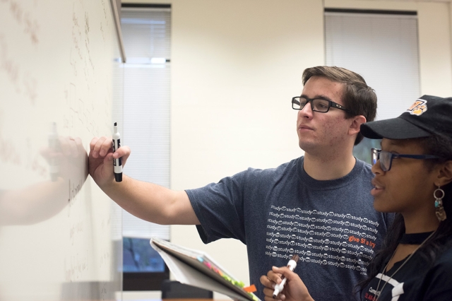 Students standing in front of a white board while they work with different formulas.