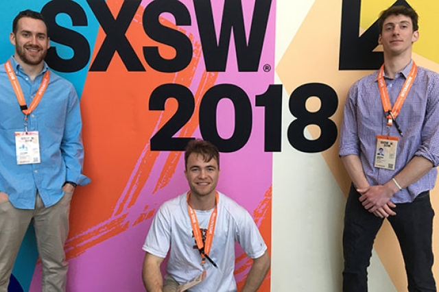 Three team members standing in front of a colorful wall that says "SXSW 2018".