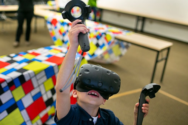 A child using a virtual reality headset and controllers at Imagine RIT.