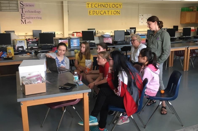 Group of middle-school students sits around a laptop computer.