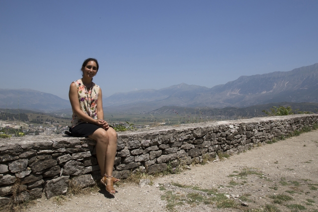 A student poses for a photo in Kosovo, on a brick wall.