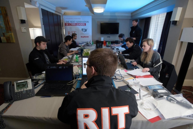 Team of students sits around table with computers and paperwork.