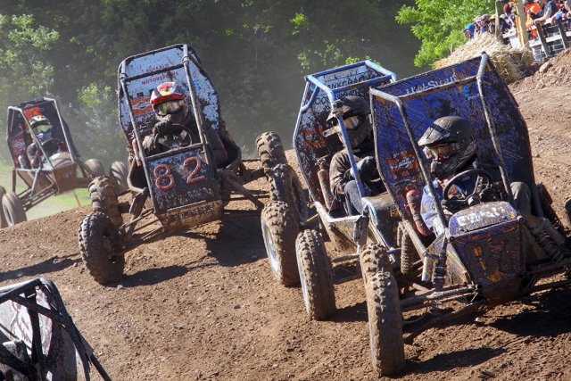 Four Baja cars race down dirt hill.