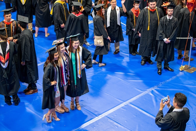 Students in graduation caps and gowns pose for photo.