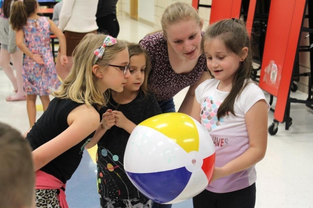 College student and three elementary school students look at beach ball.