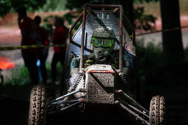 Head-on view of baja car and driver covered in mud.