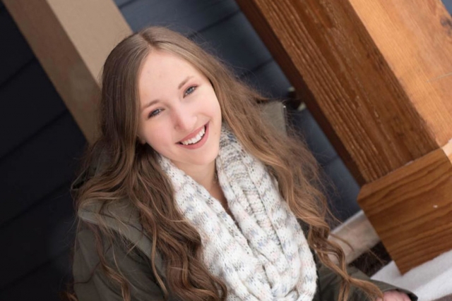 Teen with long brown hair, green jacket and knit scarf.